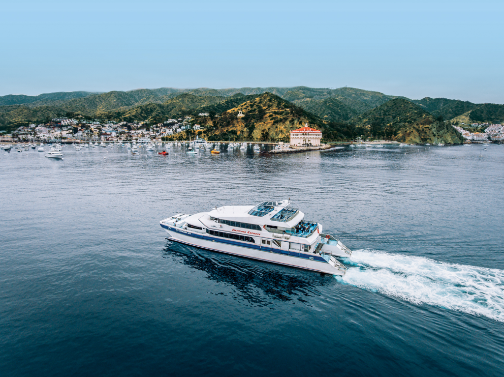 A Catalina Express ferry crossing toward Avalon, with the town and the island hills behind it.